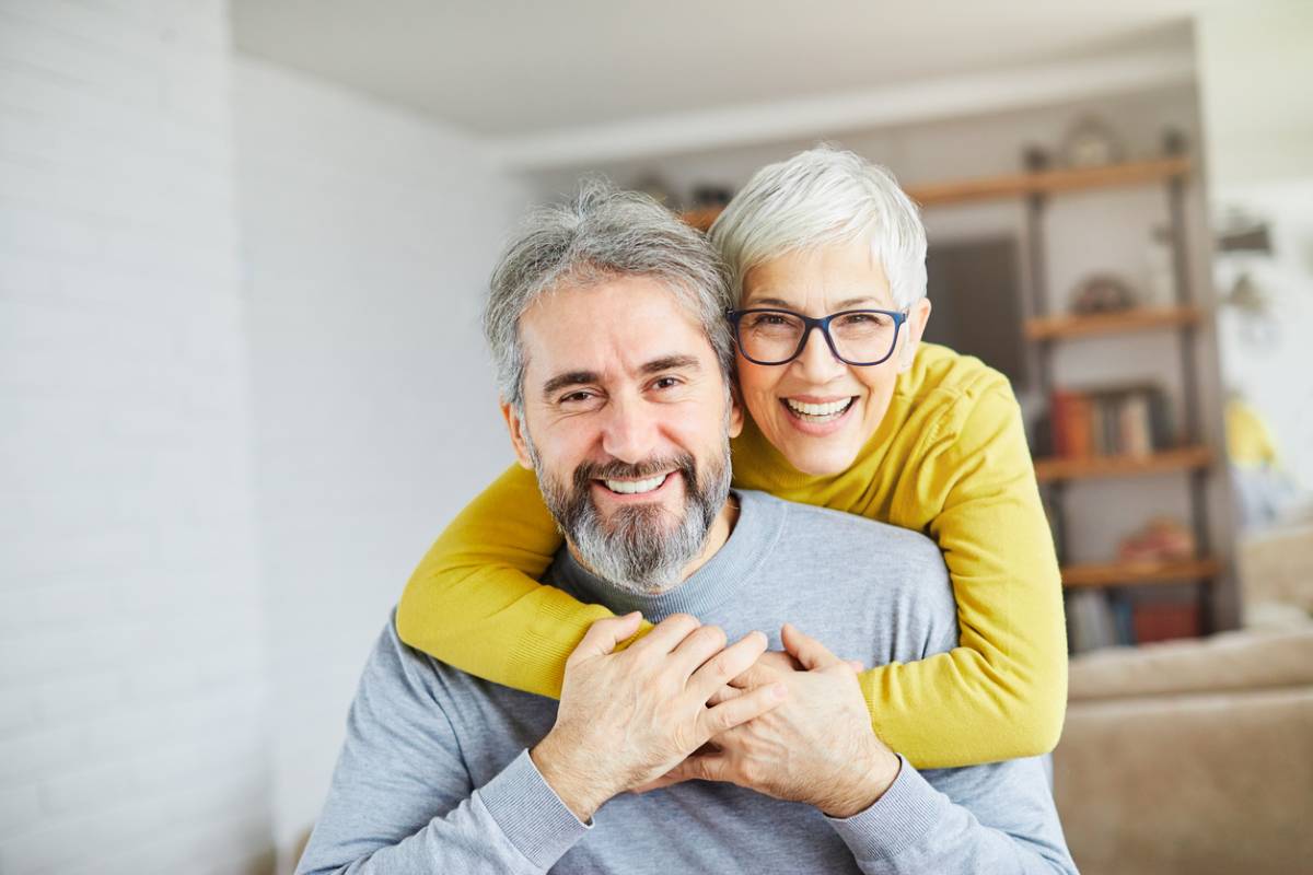 Stock image of older couple smiling with woman behind man arms wrapped around him